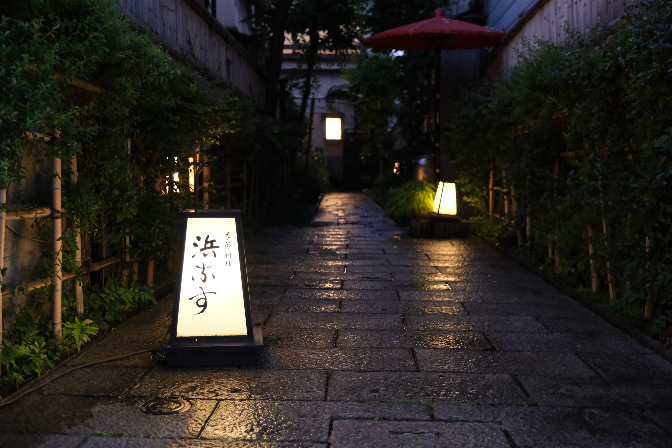 夕暮れの花小路。濡れた石畳に行灯の明かりが灯る浜なすへのアプローチ